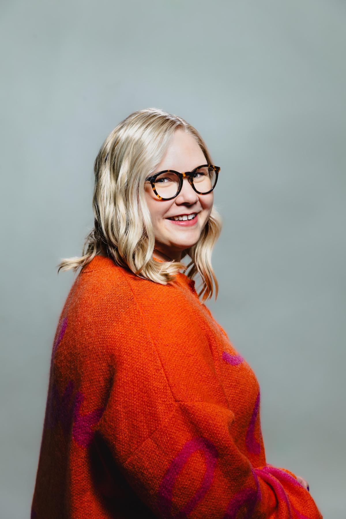 Blond kvinna med orange tröja och glasögon