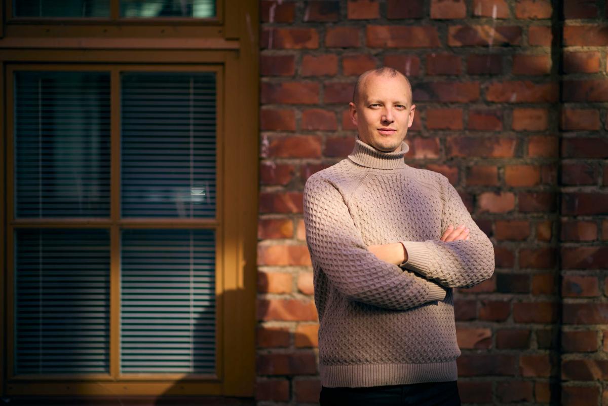 Författaren Simon Ventus står med armarna i kors framför en röd tegelvägg. Foto: Linus Lindholm