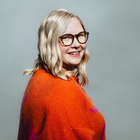 Blond kvinna med orange tröja och glasögon
