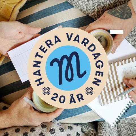 Sedd från ovan: Två par händer motsatt varandra håller i en kaffekopp och anteckningsblock och pennor. En mans huvud med en röd mössa och skäggiga ansikte och en gul kudde syns till vänster. Till höger en grå filt. På mitten är Marthaförbundets m-logo på en blå bakgrund i en cirkel. Runt den texten: Hantera vardagen 20 år. Under det ett blåvitrandigt tyg, kanske en soffa som personerna sitter på.