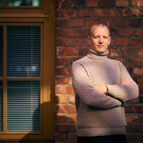 Författaren Simon Ventus står med armarna i kors framför en röd tegelvägg. Foto: Linus Lindholm